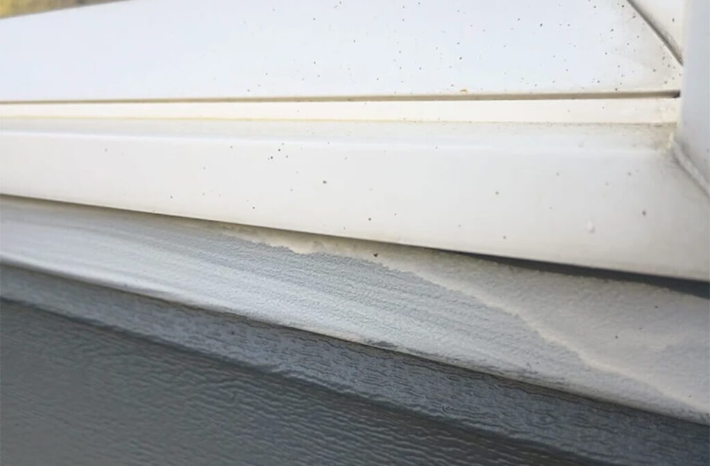 A close-up view of a window frame where the paint is peeling and has some dirt accumulation.